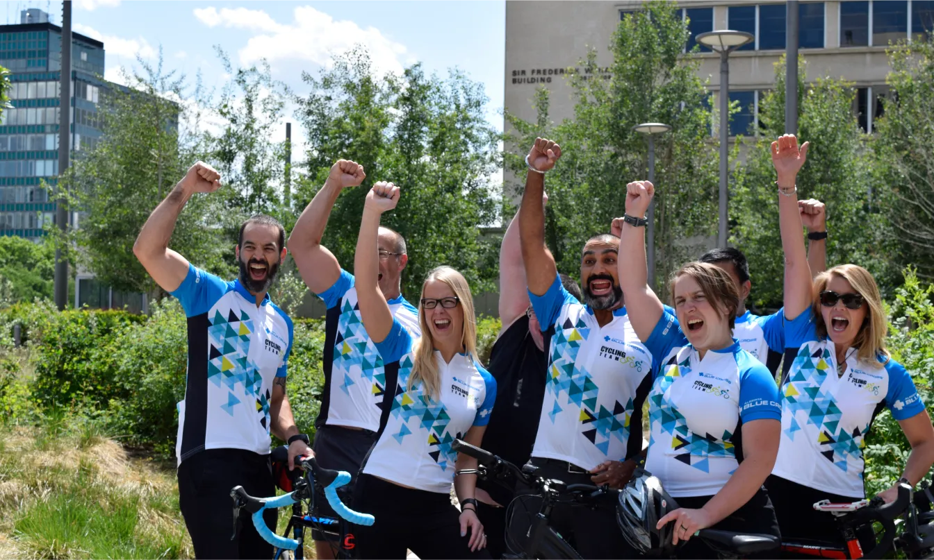 A group of people wearing matching jerseys raise their fists in celebration while standing outdoors next to their bikes.