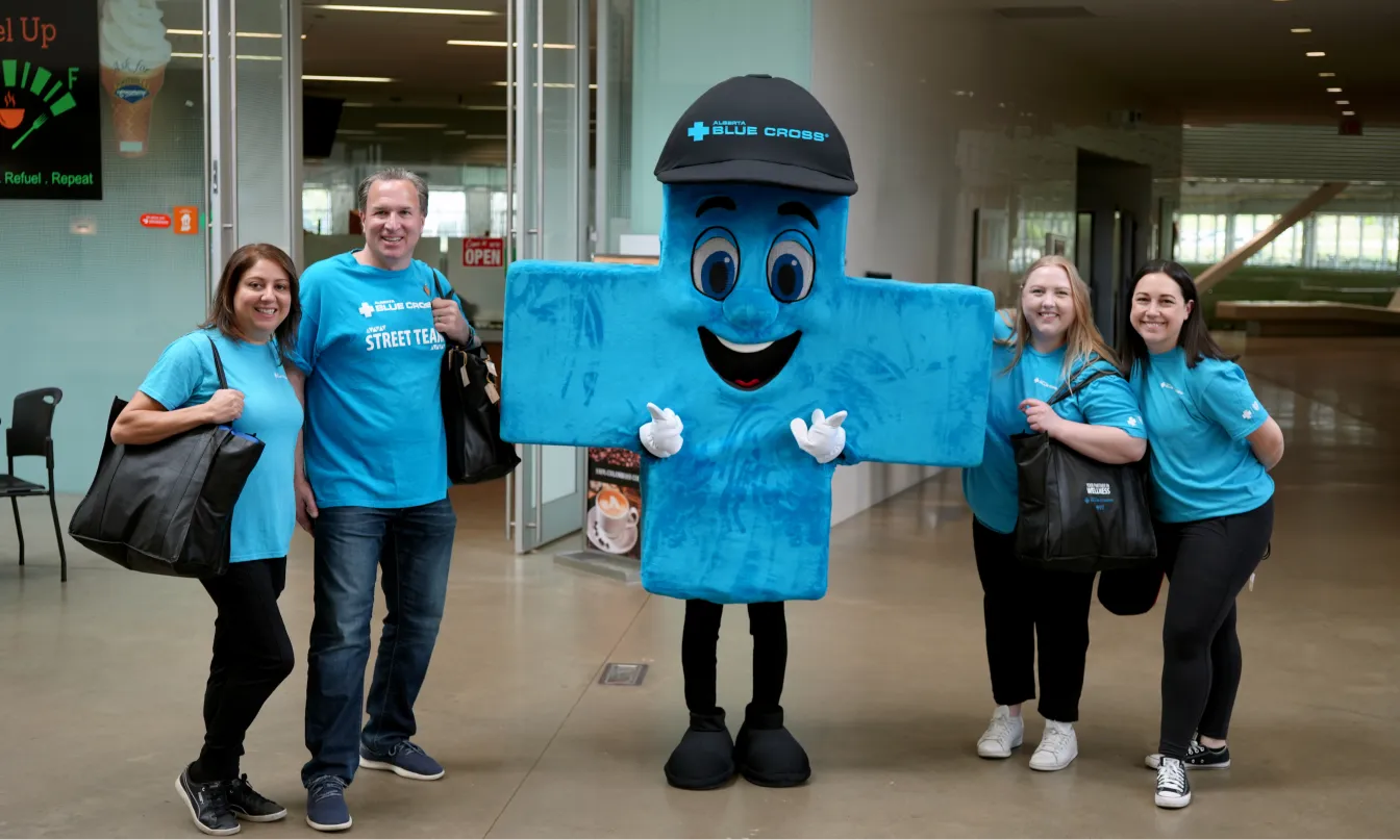 A group of employees in blue shirts smiling while posing with a blue Alberta Blue Cross mascot.