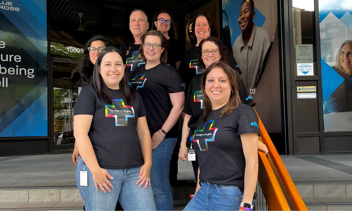 A group of employees standing on the stairs outside the Alberta Blue Cross office building, wearing Pride t-shirts.